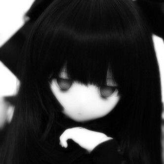 A black and white, slightly blurred image of an anime-esque doll. The doll had black hair with blunt bangs covering its forehead. Its eyes are dark grey and it looks tired/unamused. The doll's skin is pure white. Its hand is just under its chin and it is l